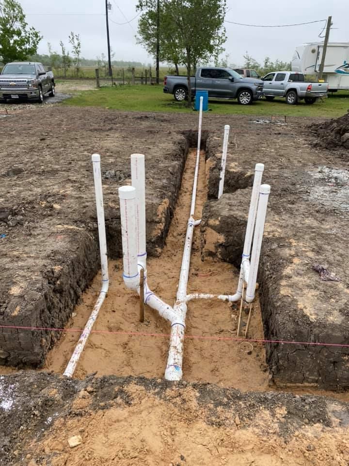 Trenched utility piping and white PVC pipes installed in a muddy excavation site.