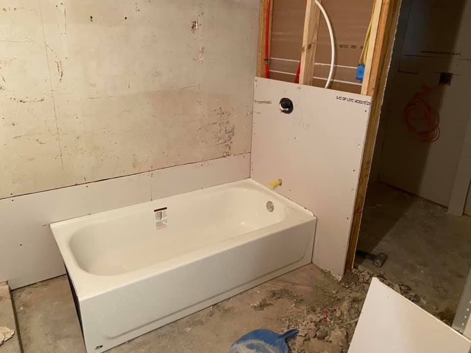 Unfinished bathroom with a white bathtub, exposed plumbing, and construction debris on the floor.