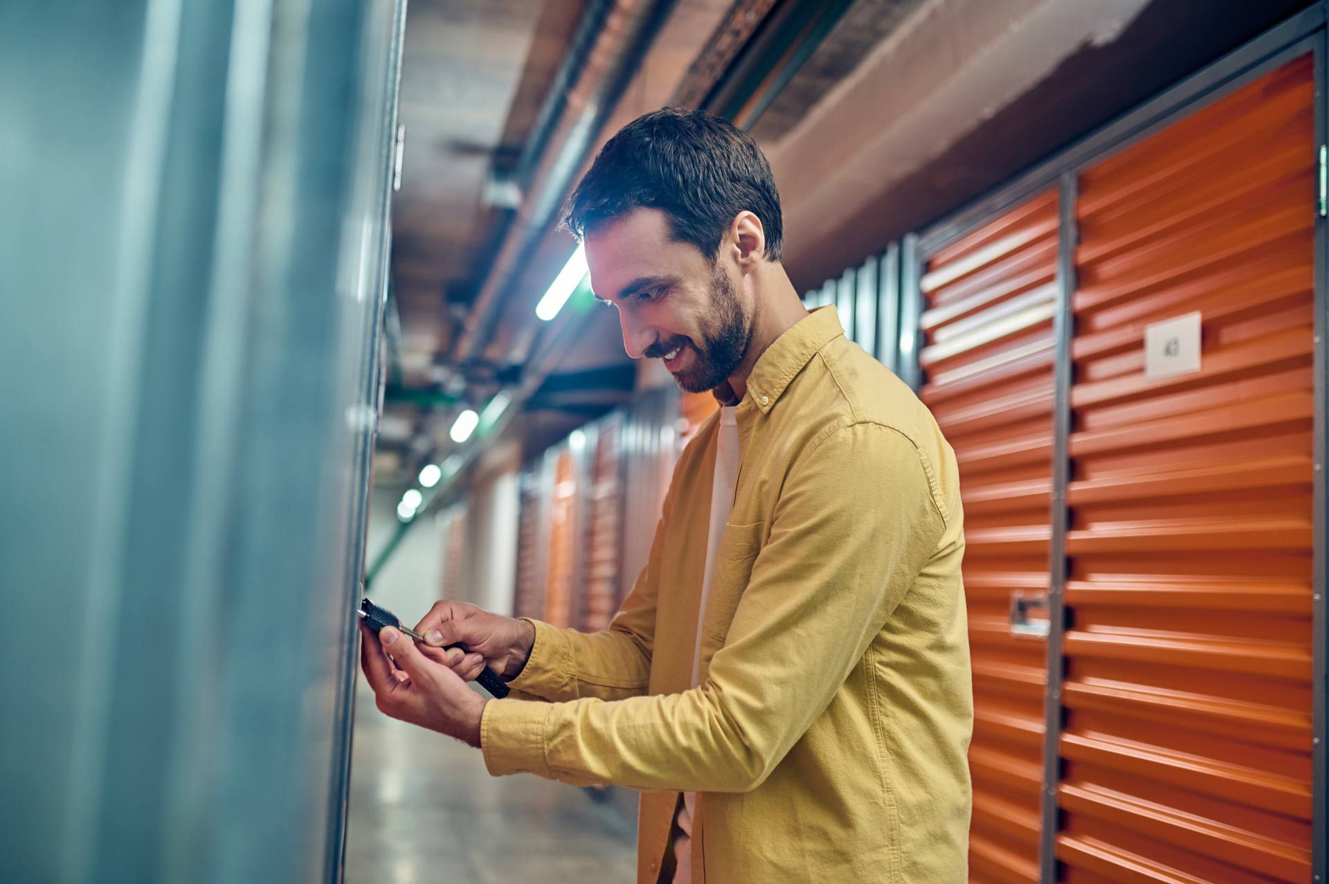 Man smiling at his phone in a storage unit hallway, wearing a yellow shirt.