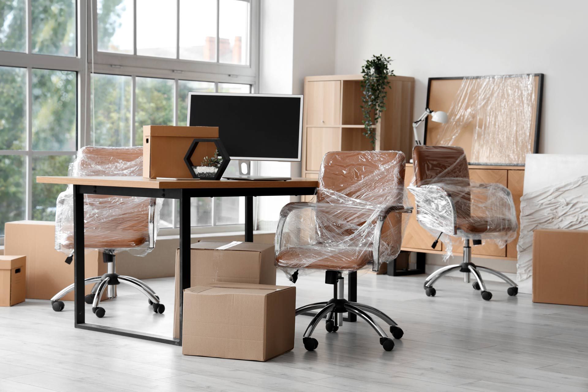 Office interior with furniture, boxes, and a computer, all wrapped in plastic for moving.