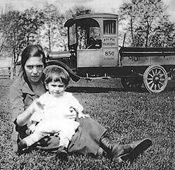 Woman and child sit on grass near truck.
