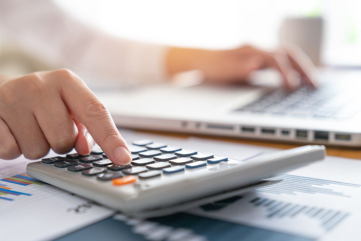A person is using a calculator in front of a laptop computer.