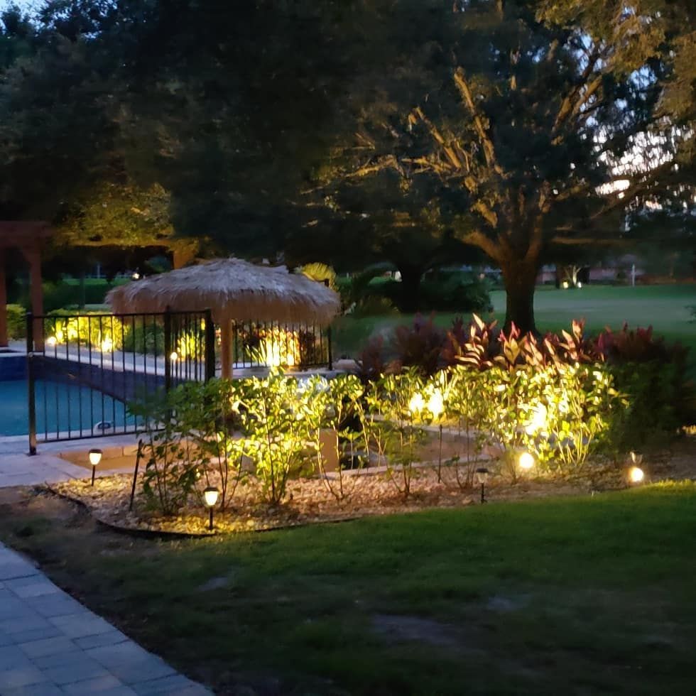Nighttime landscape with illuminated garden beds and pool area.