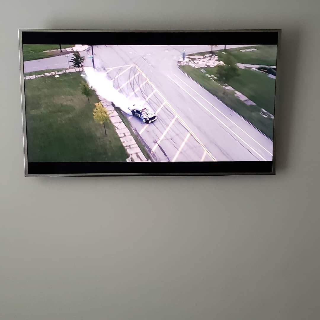 TV displaying an aerial view of a truck emitting a white cloud, driving on a road next to a grassy area.