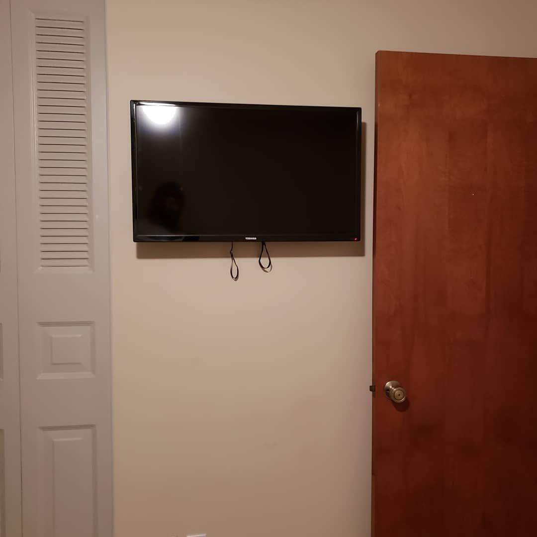 A TV is mounted on a beige wall next to a wooden door and a white closet.