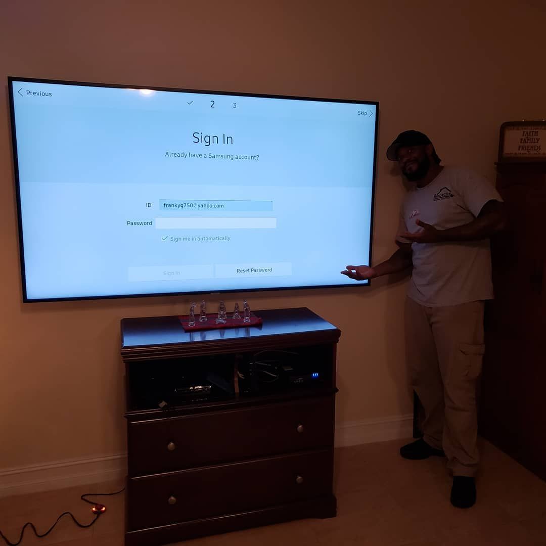 Man points to mounted TV screen displaying a sign-in prompt above a wooden cabinet.