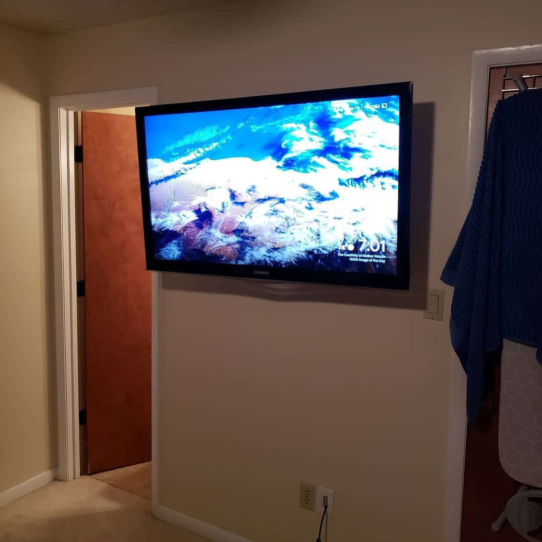 A flat-screen TV mounted on a beige wall; a door and a closet are visible nearby.