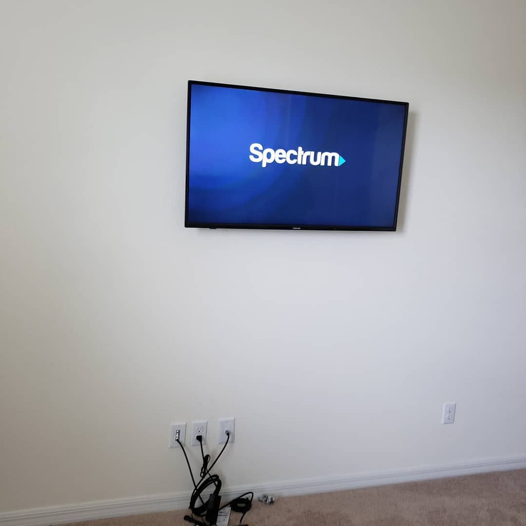 A wall-mounted TV displaying the Spectrum logo above a tangle of cords and outlets.