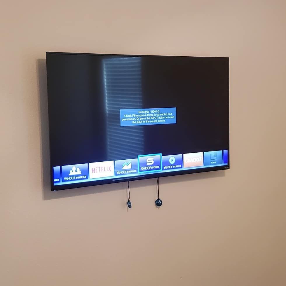 Wall-mounted TV with a blue menu on screen, cables hanging below. The wall is beige.