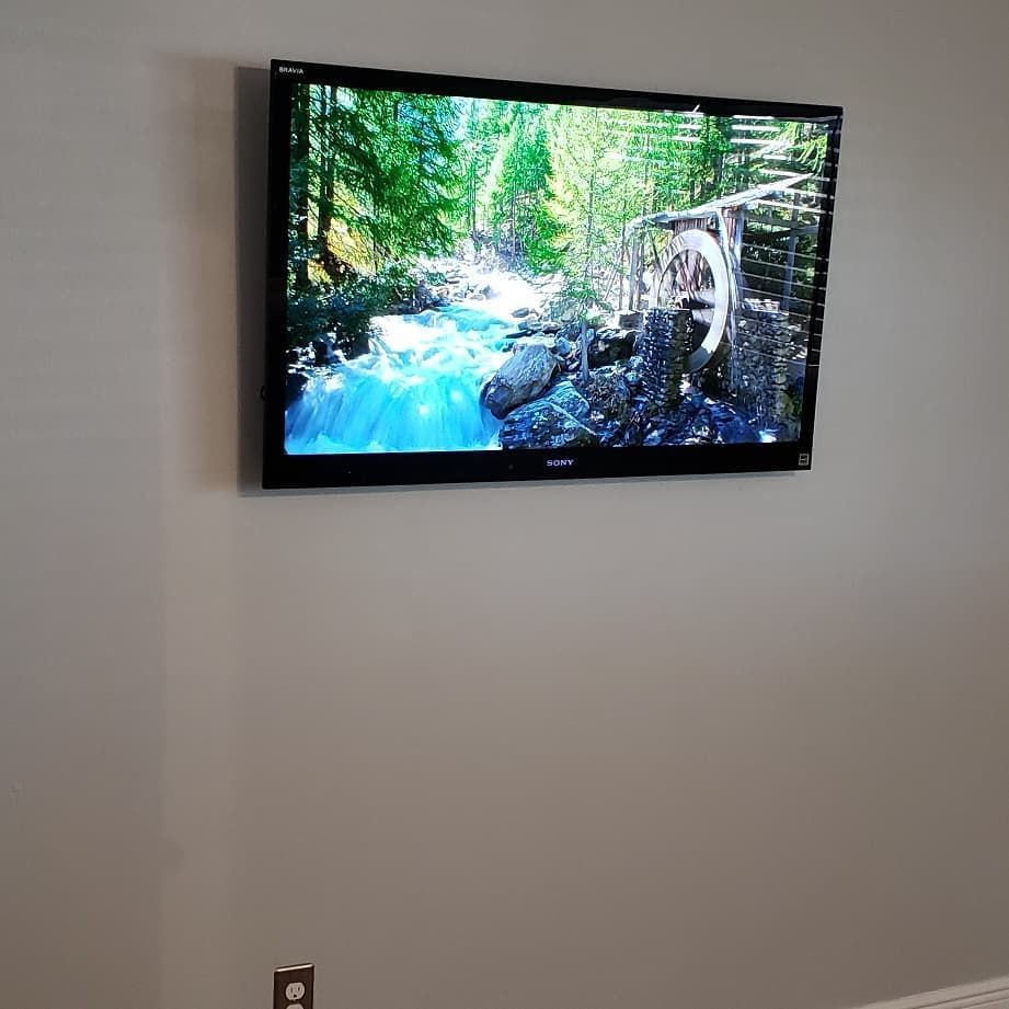 A flat-screen TV mounted on a gray wall, displaying a video of a river scene.