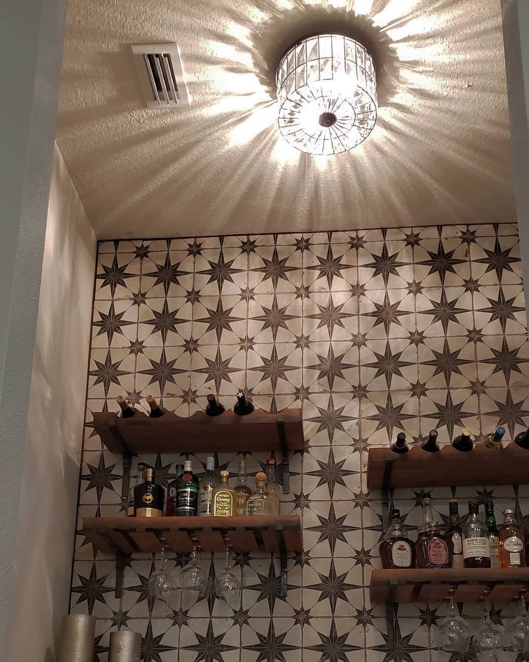 Bar area with star-patterned tile, wooden shelves holding bottles, and a patterned light fixture on the ceiling.
