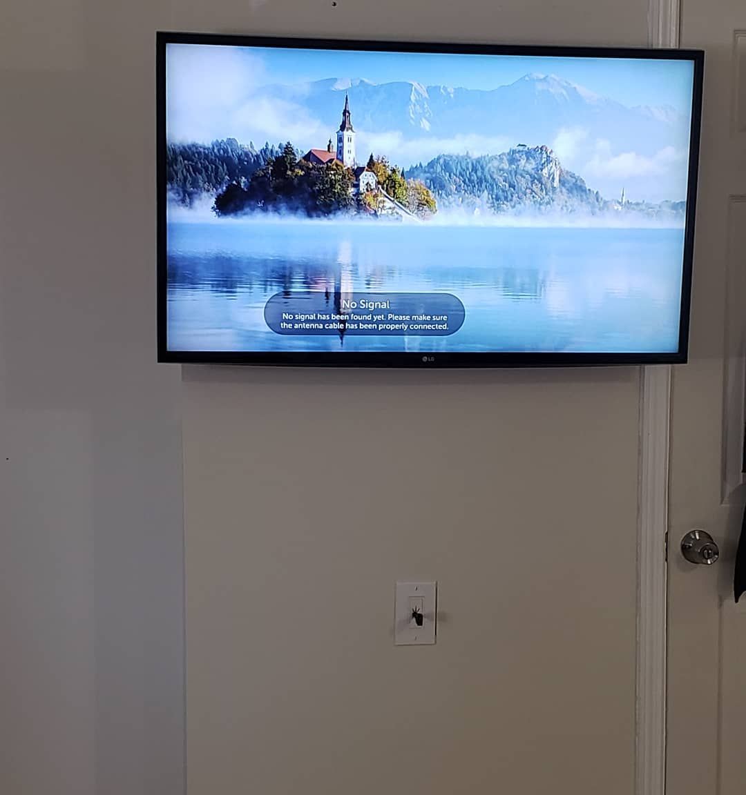 A flat-screen TV mounted on a light-colored wall displays a landscape over a lake.