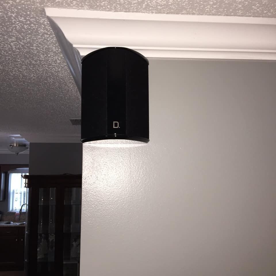 Black speaker mounted on a white wall below crown molding; open doorway to the left.