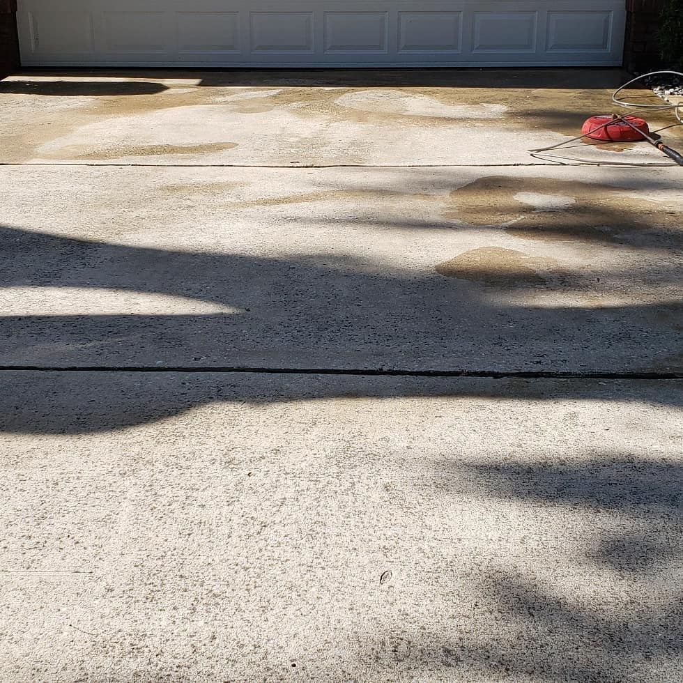 Concrete driveway with shadow and garage door in the background. A cleaning tool rests on the right.