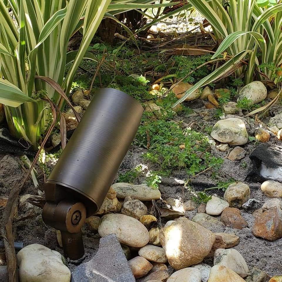 Bronze landscape spotlight in a garden bed with rocks and plants.