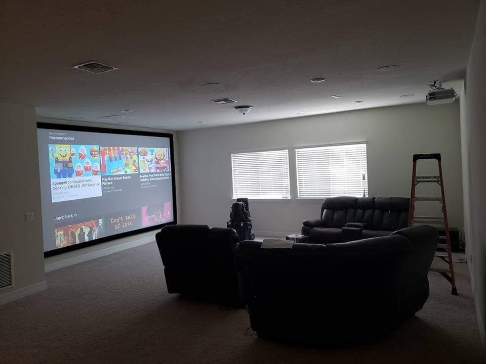Home theater room with a large screen displaying a streaming service, dark seating, and a projector.