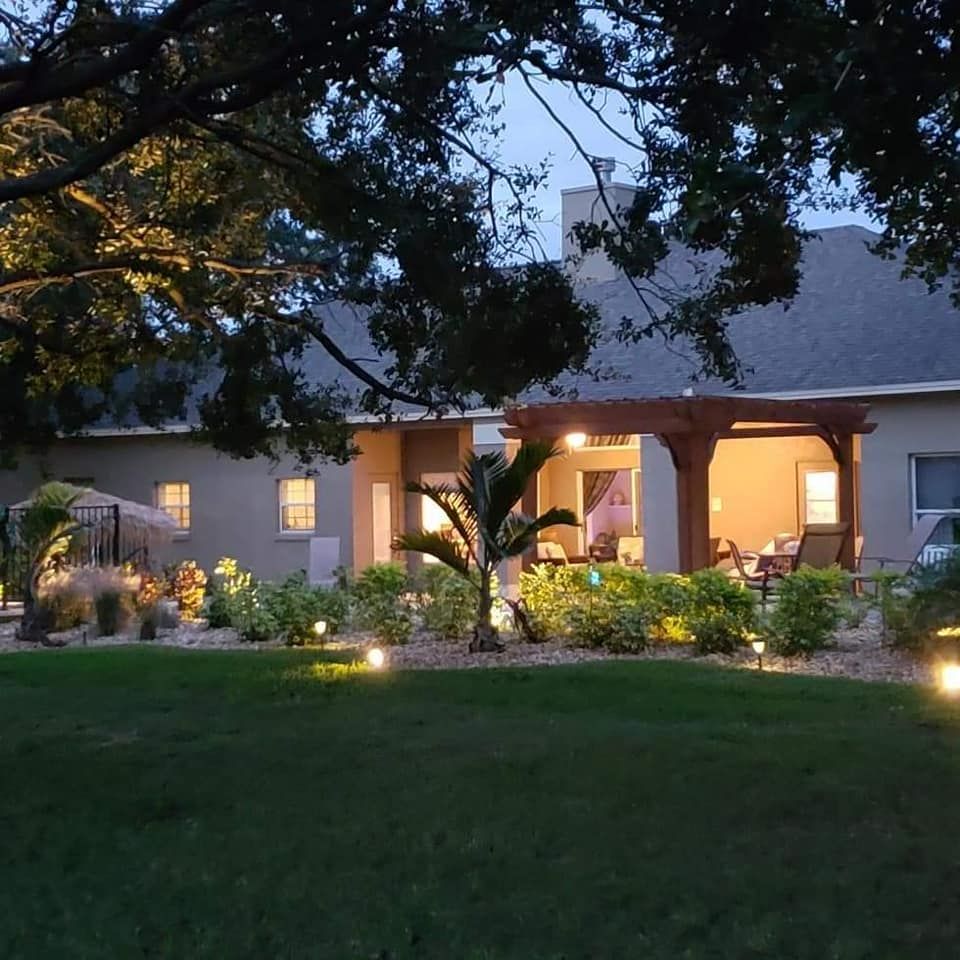 Night view of a house with lit outdoor landscaping. Low lights illuminate bushes and a patio with a pergola.