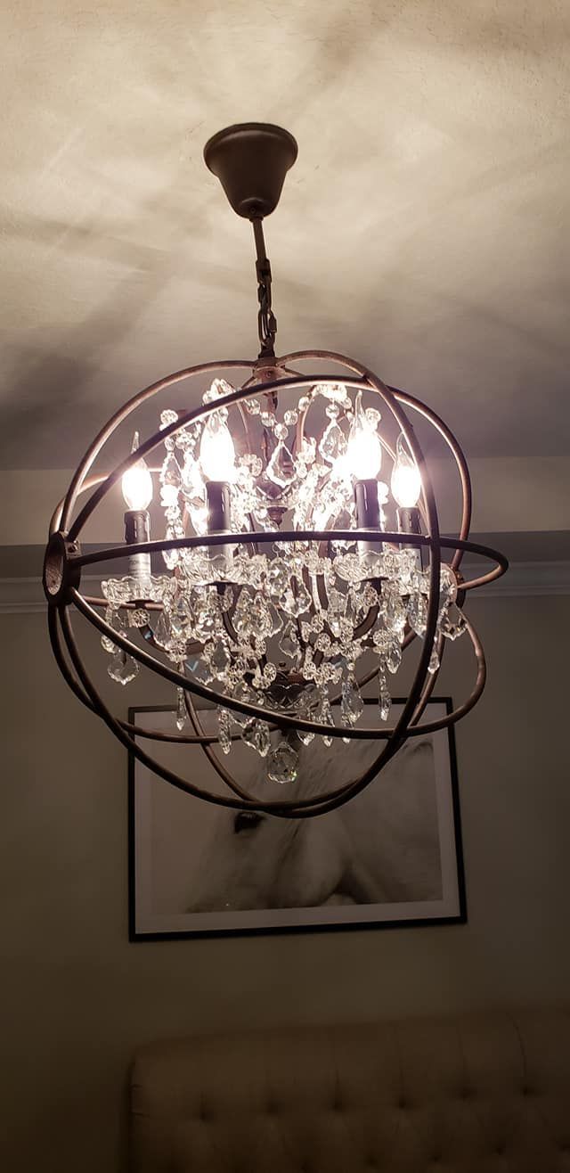 Chandelier with crystal accents, dark metal frame, hanging above a framed picture on the wall.