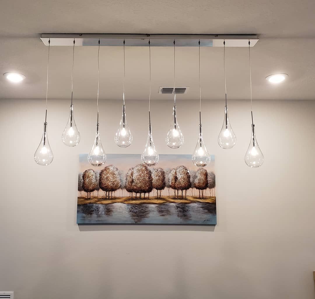 Modern dining room chandelier with teardrop lights above a landscape painting.