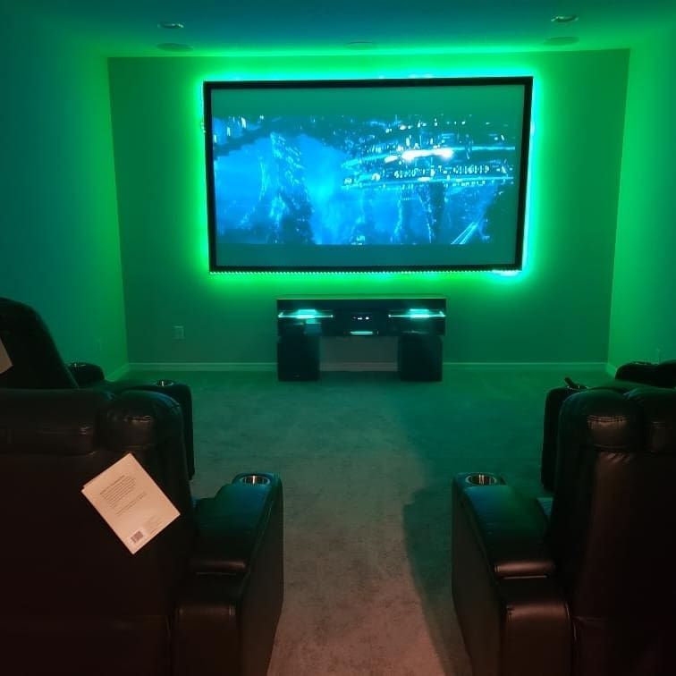 A home theater with a screen, speakers, and black leather recliners. A projector is mounted on the ceiling.