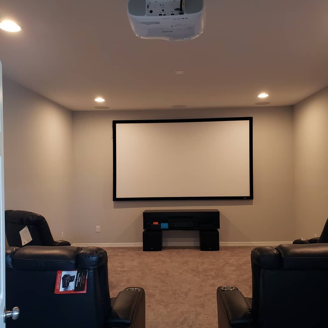 Black wall-mounted speaker with a downward-facing light on a white wall, near a ceiling with crown molding.