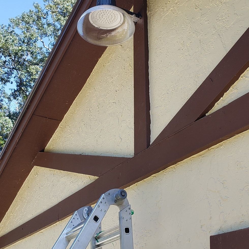 Exterior wall with brown trim, beige stucco, a security light, and a ladder.