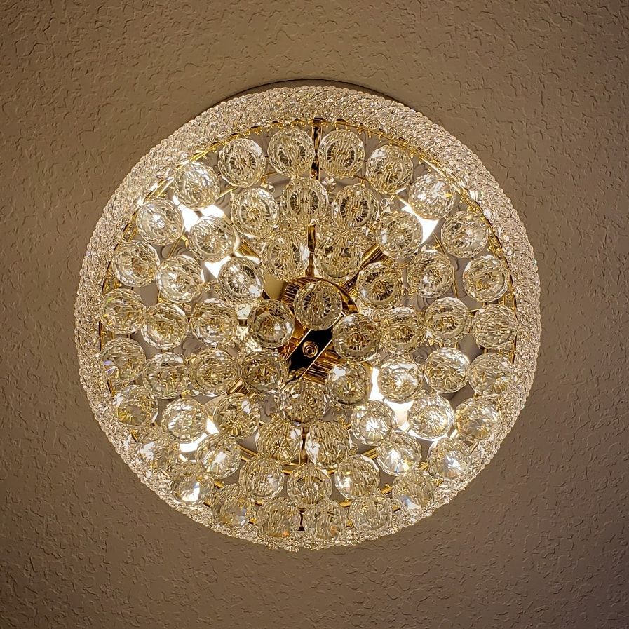 Round, ornate ceiling light fixture, studded with numerous clear crystal-like baubles.