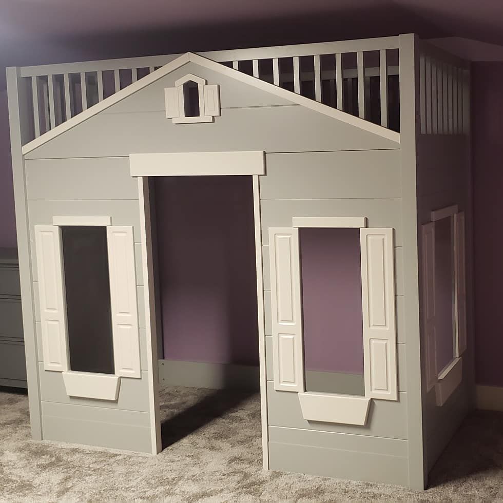 Gray playhouse bed with white trim; open doorway, shuttered windows, balcony with railing, set against purple wall.