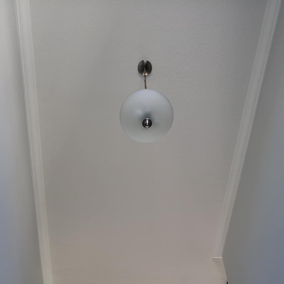 White ceiling with a round, frosted glass light fixture hanging from a silver mount.