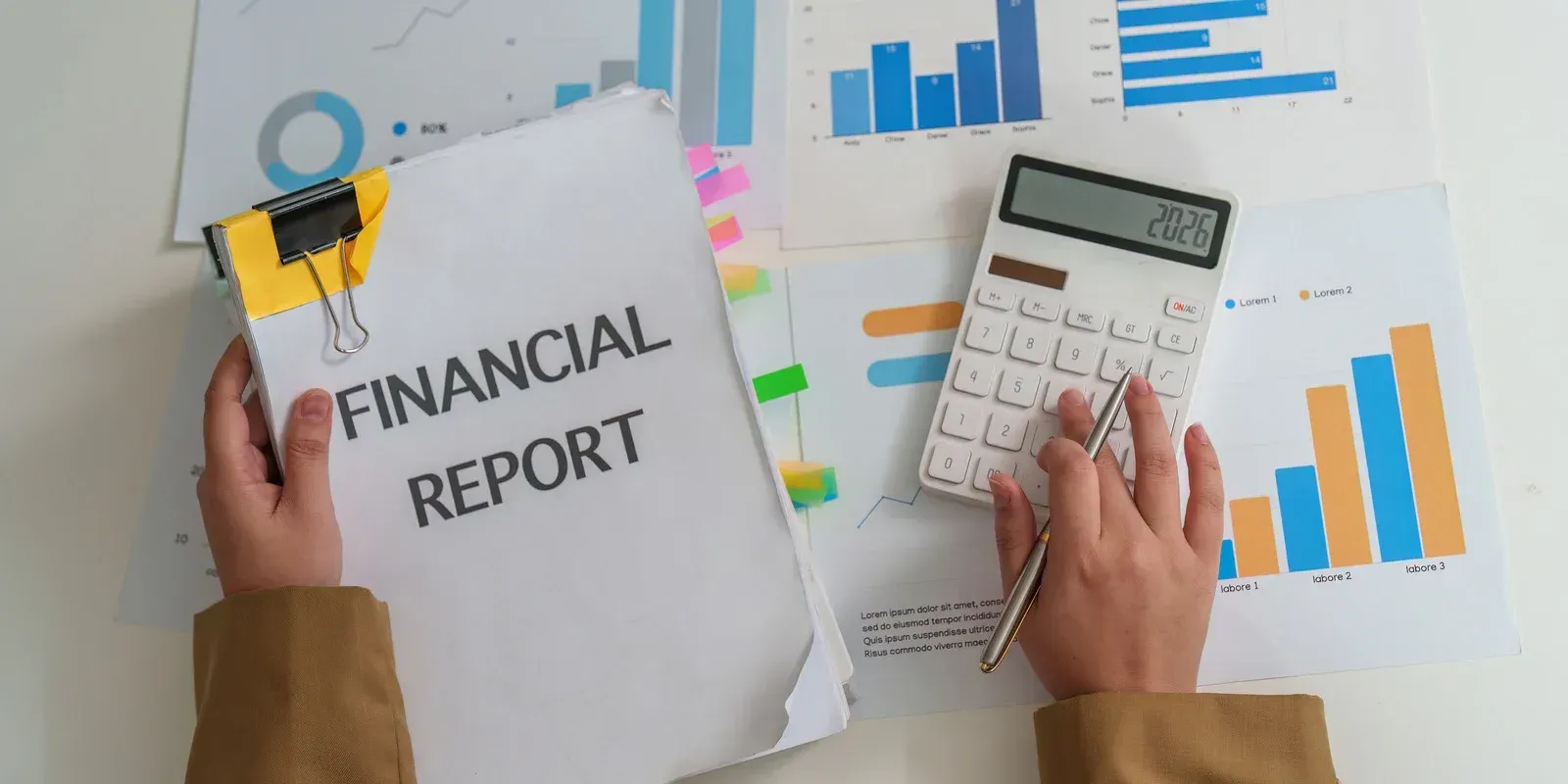 Person calculating finances with calculator and financial report with graphs.