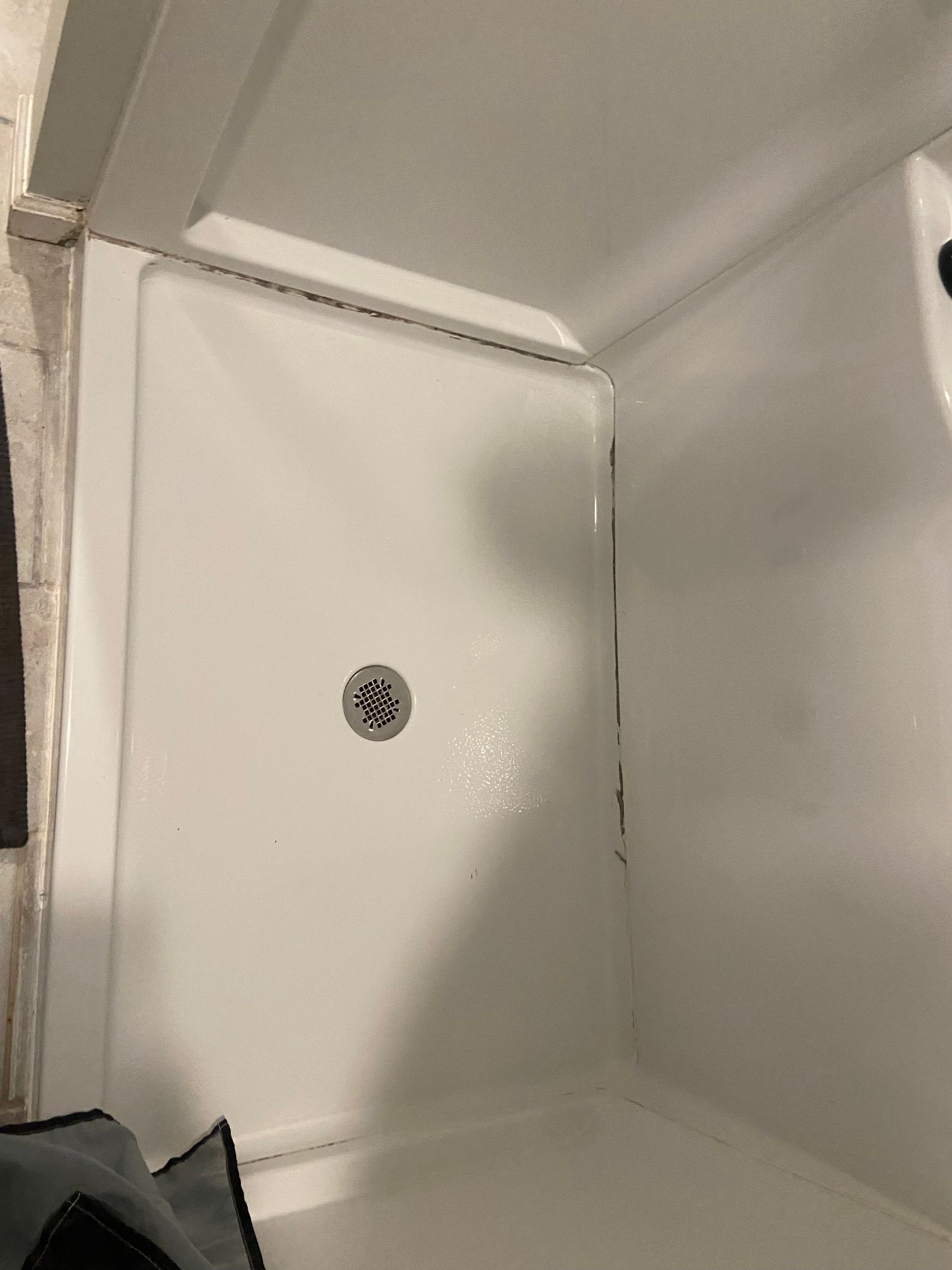 A white shower stall with a drain in a bathroom.