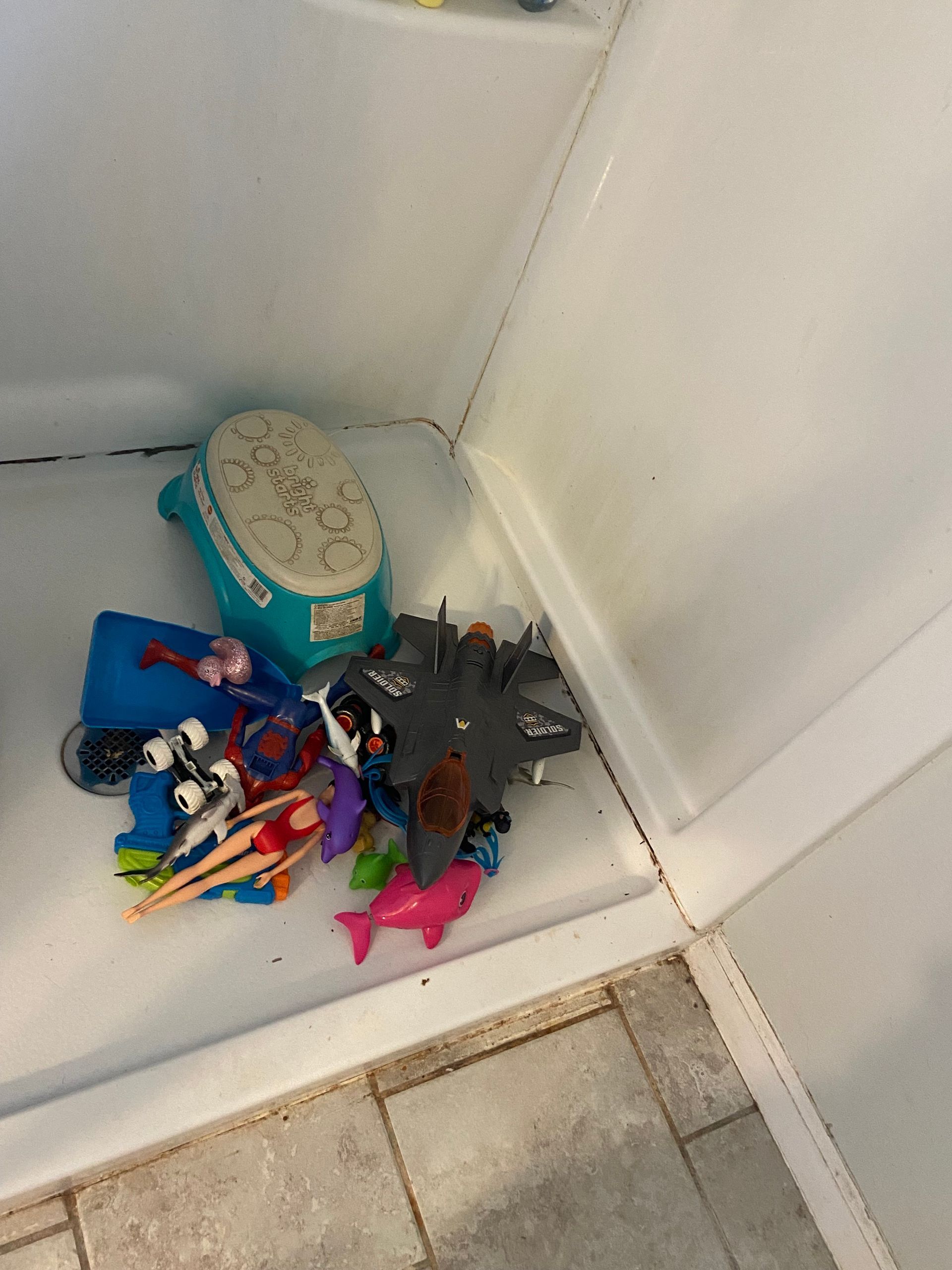 A bunch of toys are sitting on the floor in a shower stall.