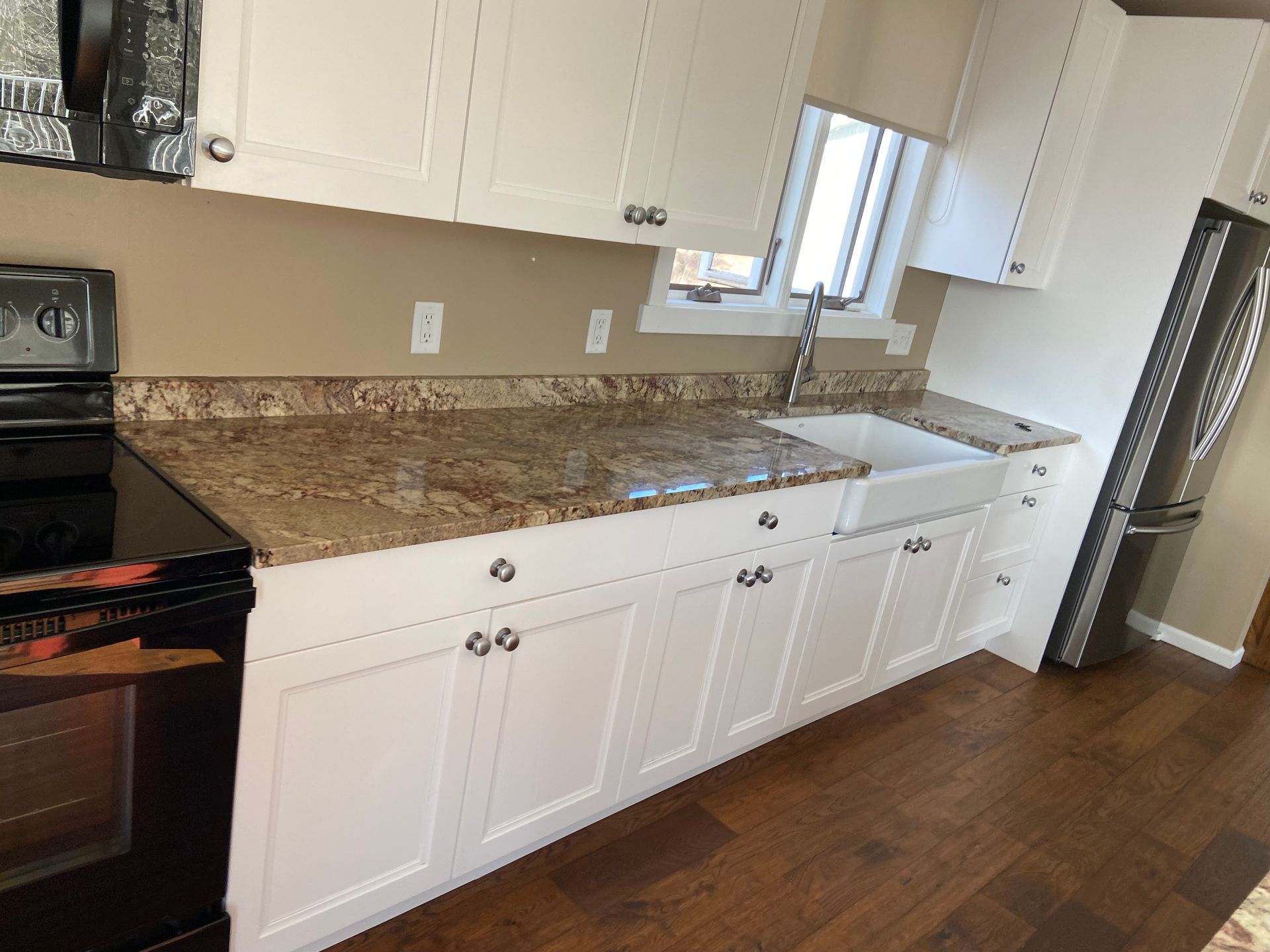 A kitchen with white cabinets , granite counter tops , a stove and a refrigerator.