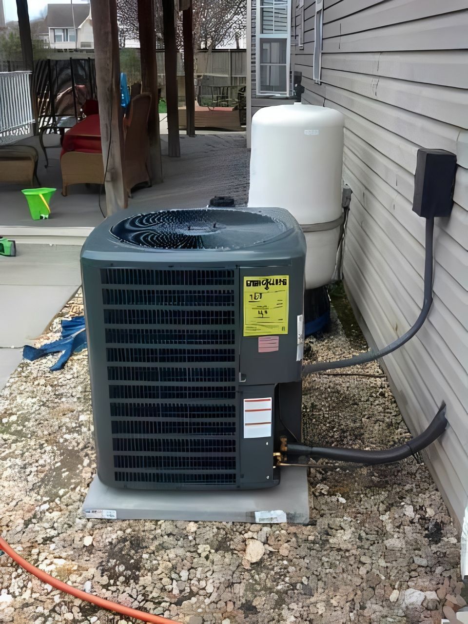 Two technicians repairing an outdoor air conditioning unit mounted on a building wall.