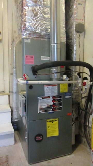 Furnace unit in a utility room. Gray metal with ductwork, vents, and warning labels.