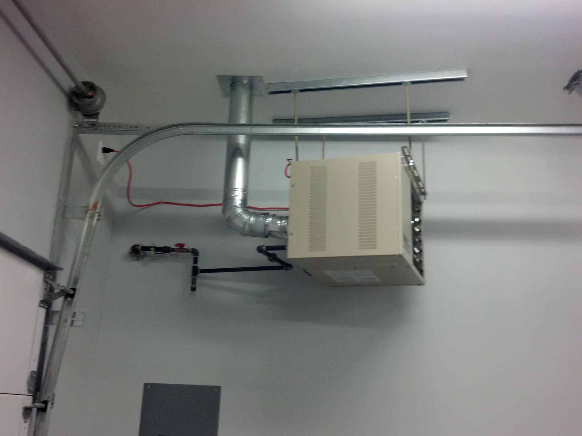 Garage ceiling with a suspended heater, exhaust vent, gas line, and door track.