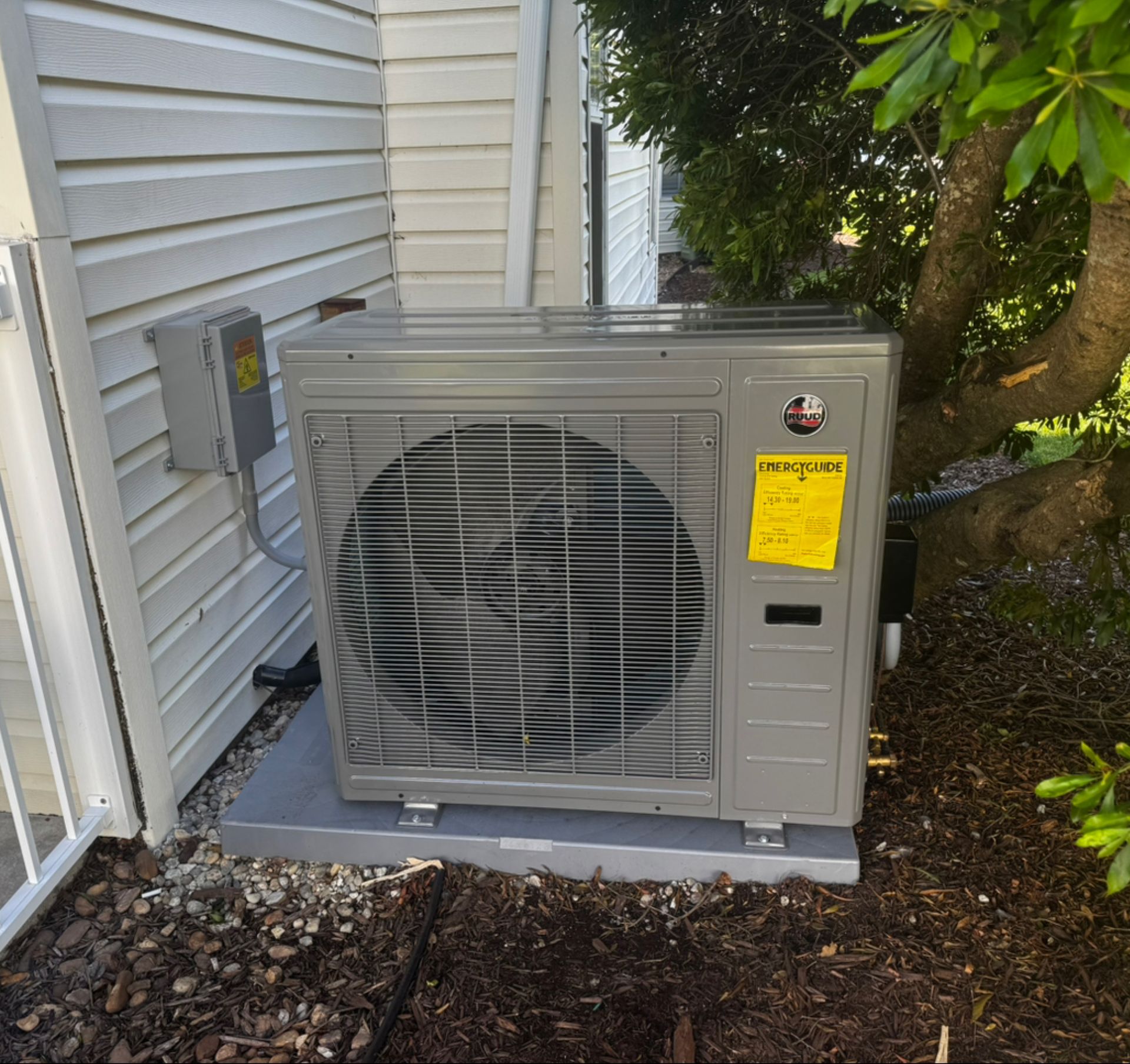 Exterior AC unit on a concrete pad next to a building with a tree in the background.