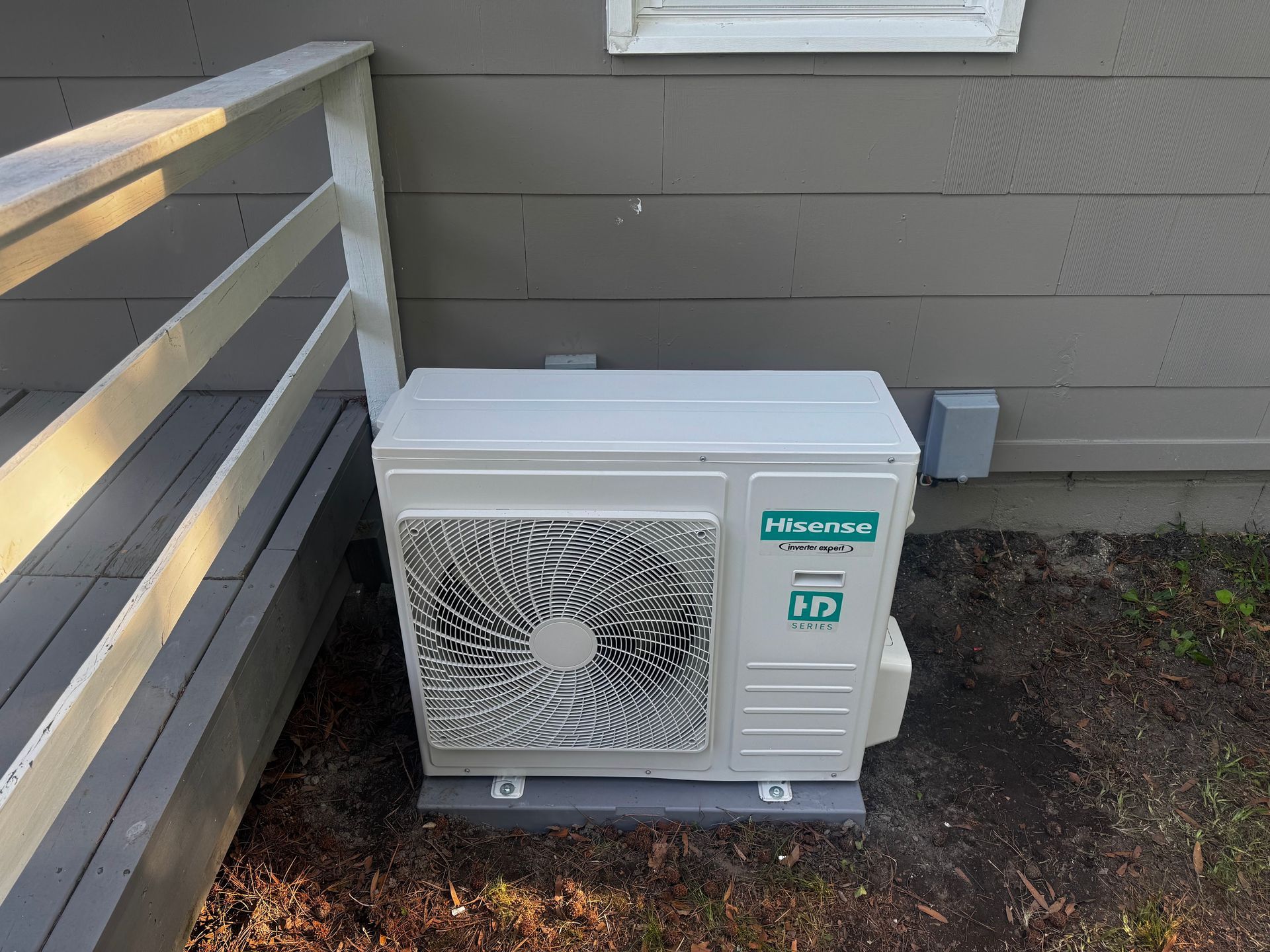 White and gray air conditioning unit on a concrete pad next to a house with a deck.