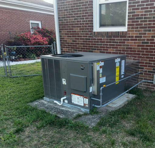 Central air conditioning unit on a concrete pad, next to a brick building and chain-link fence.