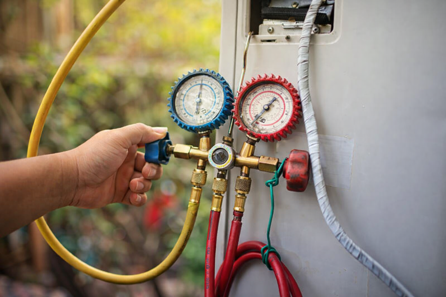 Person using gauges to check an air conditioning unit; two dials, yellow and red hoses.