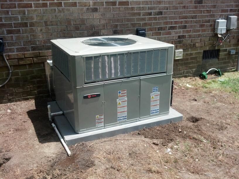 An air conditioning unit on a concrete pad against a brick wall.