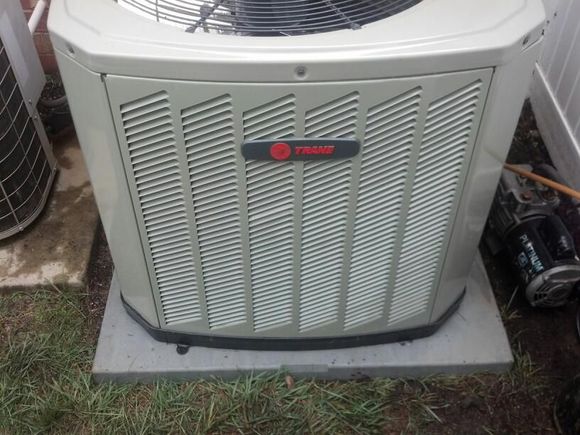 Trane air conditioner unit on a concrete pad, surrounded by grass.