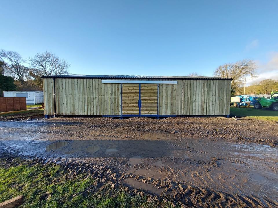 A large wooden building is sitting in the middle of a muddy field.