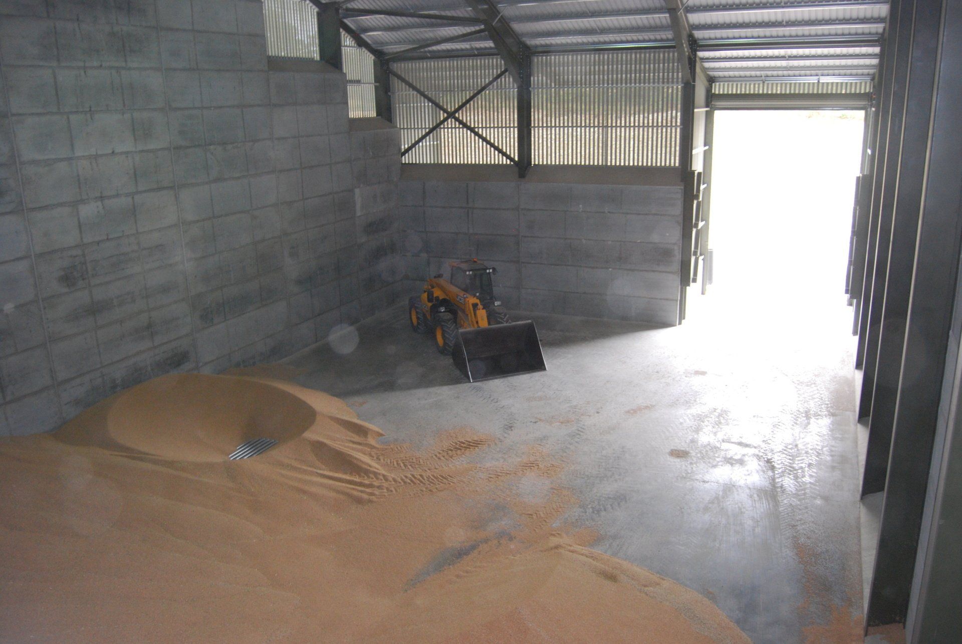 A warehouse with a lot of grain and a tractor in it.