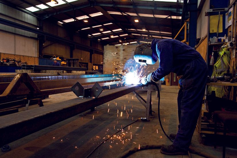 A man is welding a piece of metal in a factory