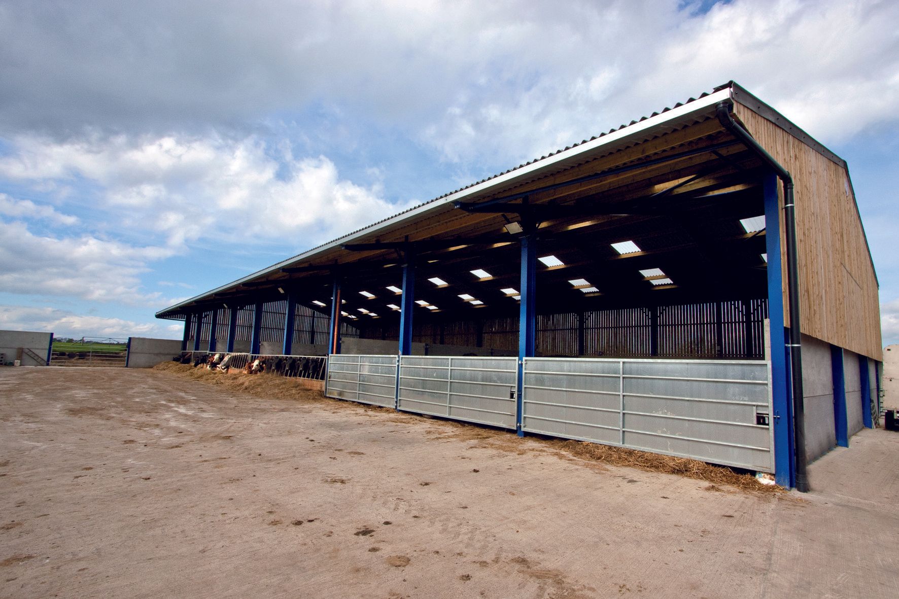 A large building with a blue roof is sitting in the middle of a dirt field.