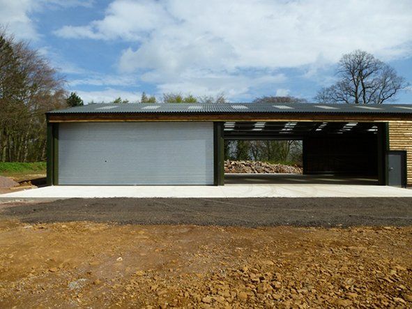 A large building with a sliding garage door is sitting in the middle of a dirt field.