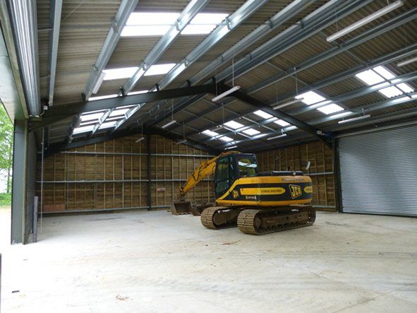 A yellow excavator is parked inside of a large warehouse.