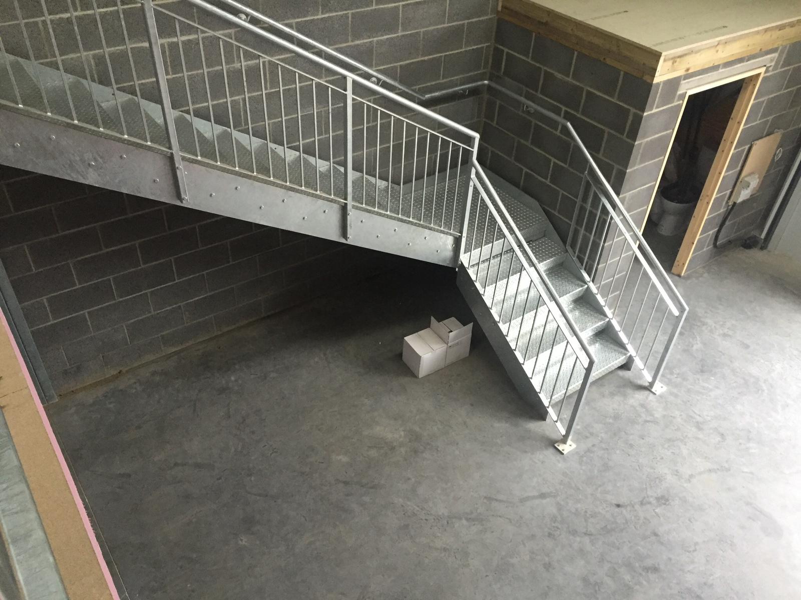 A staircase in a building with a metal railing and a brick wall.