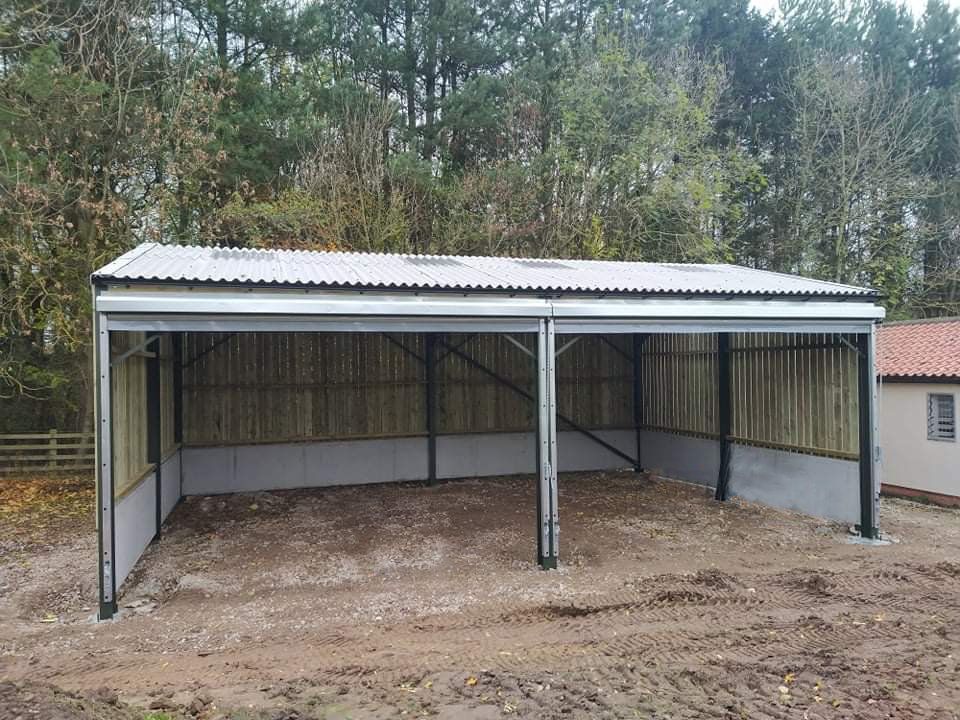 A metal building with a roof is sitting in the middle of a dirt field.